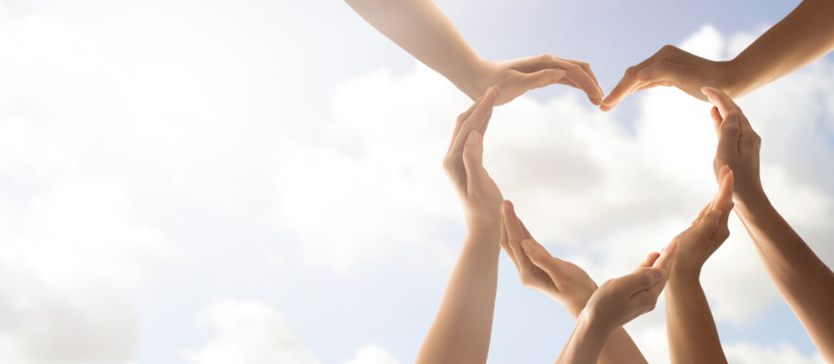 Several sets of White hands forming a heart against light cloudy sky