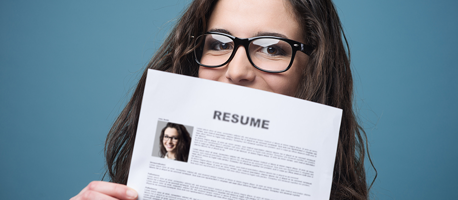 White woman in glasses covering half of face with resume with headshot