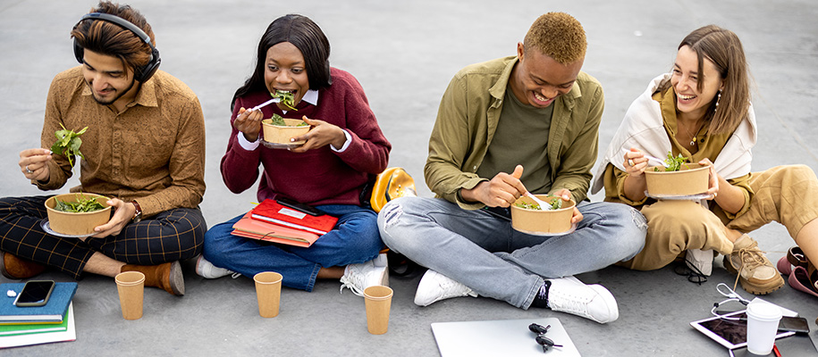 Four diverse college students sitting outside with notebooks, eating salads