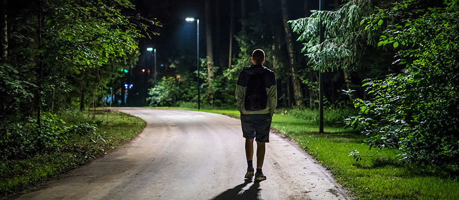 Man walking alone in shorts with backpack on campus under light posts at night