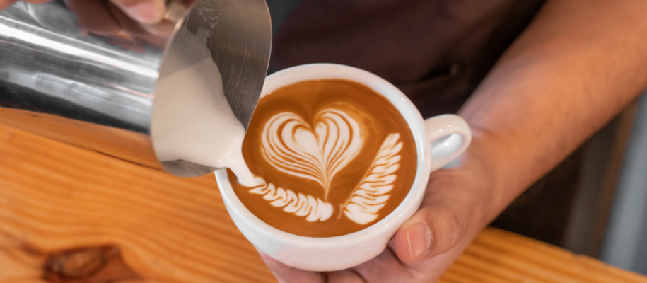 Closeup of latte with heart pattern as man's hands holds cup and pours milk in