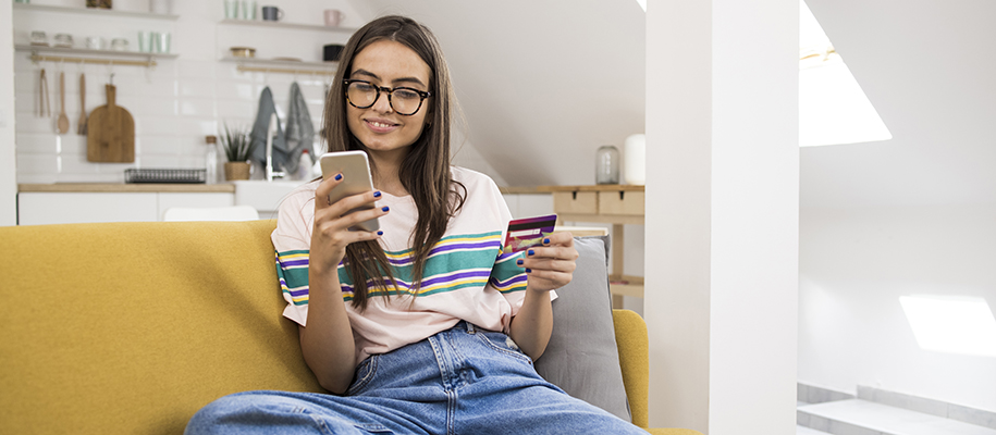 Young woman in glasses and striped shirt on couch with phone and credit card