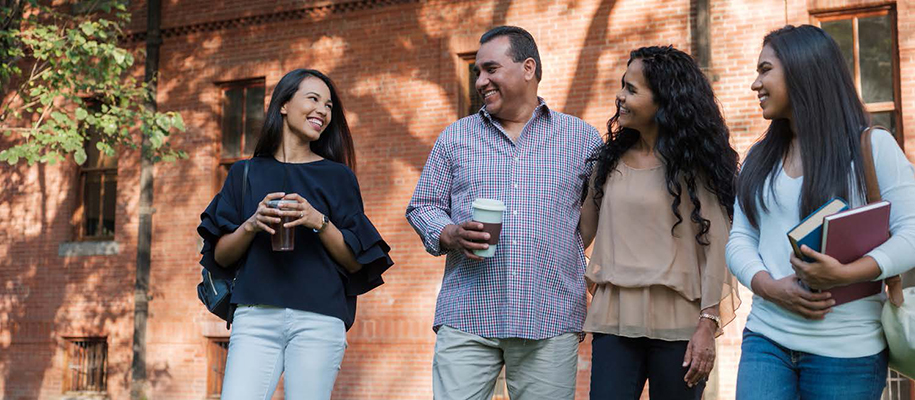 Mixed-race mom, dad, two daughters w/ coffee, bags, books outside brick building