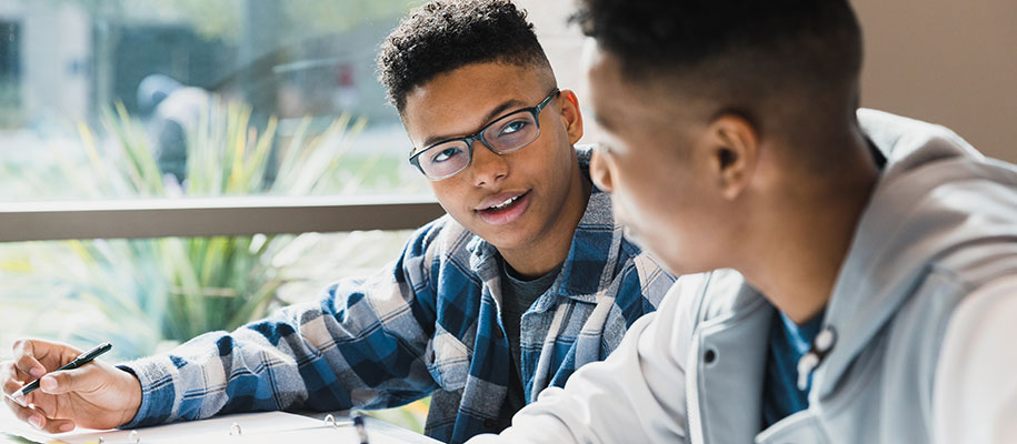 Young Black male student in glasses taking notes text to Black male classmate