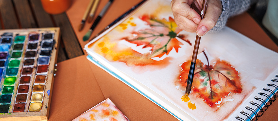 Hand of person painting fall leaves with watercolor paints