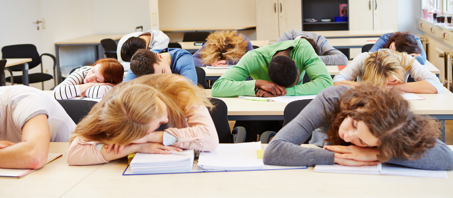 Group of students asleep in classroom with heads on desks and notebooks