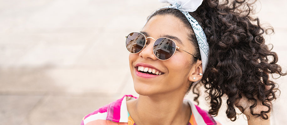 Latina teen smiling with curly brown hair, white headband, sunglasses