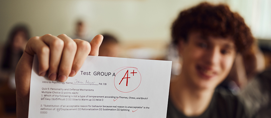 White male high school student out of focus, focus on A+ psych test he holds up