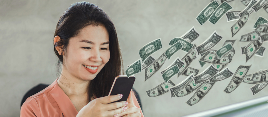 Asian female holding smartphone and smiling as dollar bills float around phone