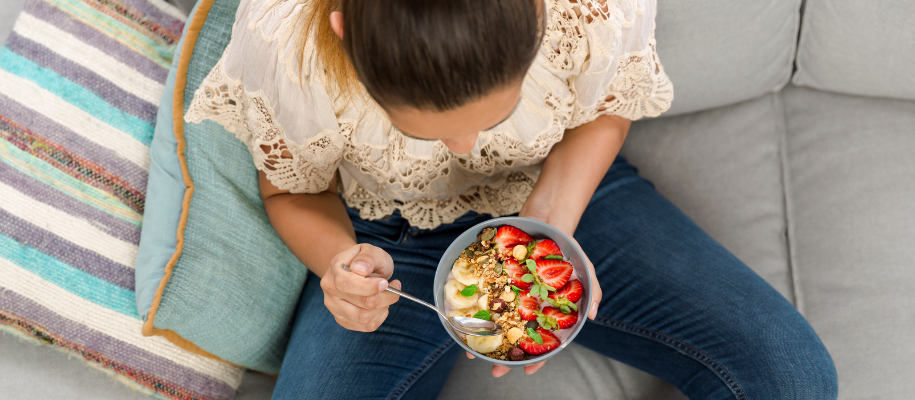 Overhead shot of White female sitting on couch eating bowl of oats and fruit