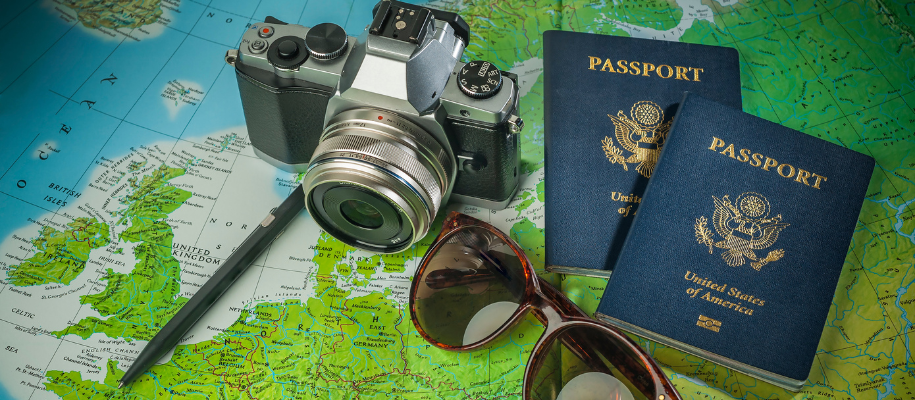 Camera, two US passports, pen, and brown sunglasses on top of European map