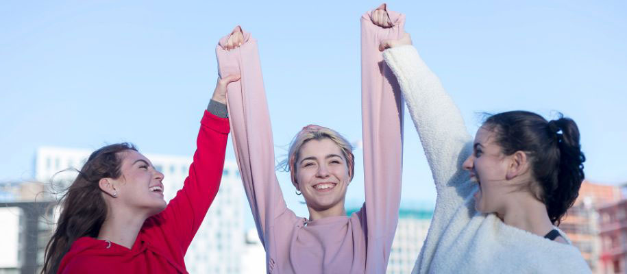 3 young White females holding hands in air excitedly, smiling and cheering