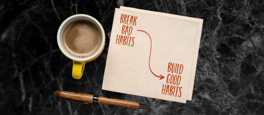 Coffee cup & pen on table with note reading Break Bad Habits, Build Good Habits