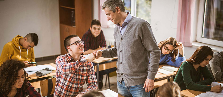 White male in glasses fist-bumping White male teacher with gray hair in class
