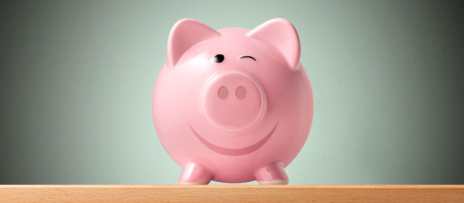 Round, pink piggy bank sitting on table in spotlight, smiling and winking
