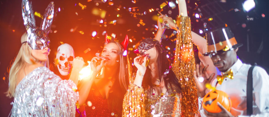 Group of young adults in Halloween costumes with party horns, confetti falling