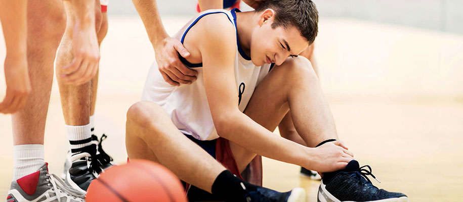 White male basketball player gripping ankle in pain surrounded by teammates