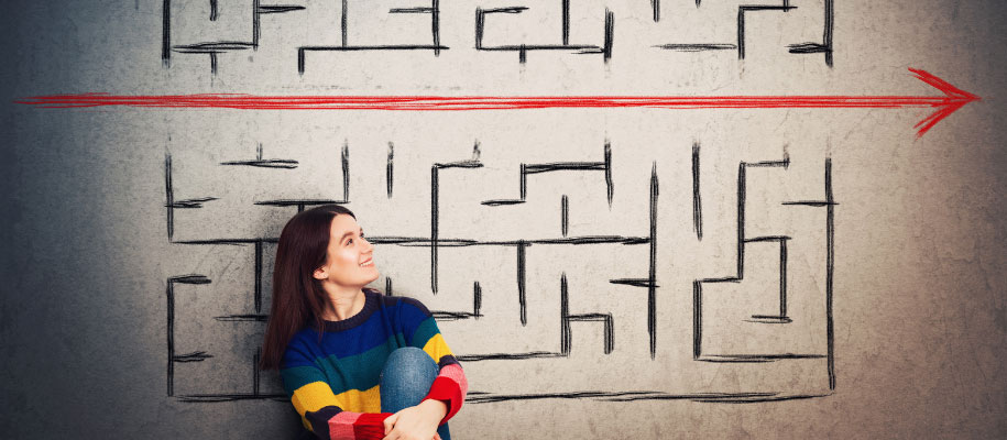 Brunette in rainbow shirt looking up at maze with straight arrow cutting through