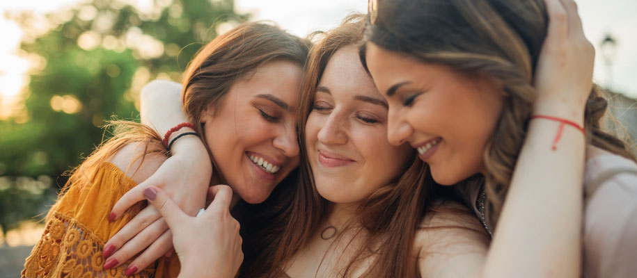 Three female friends embracing, smiling, and closing eyes outside