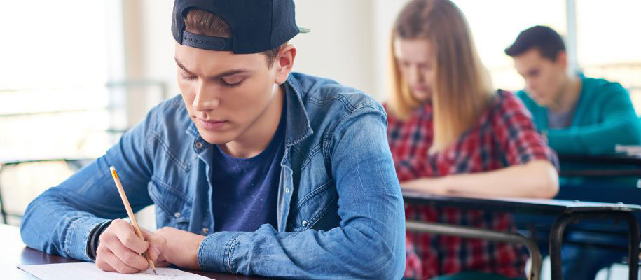 Teenage male in backwards cap taking exam at desk with other students
