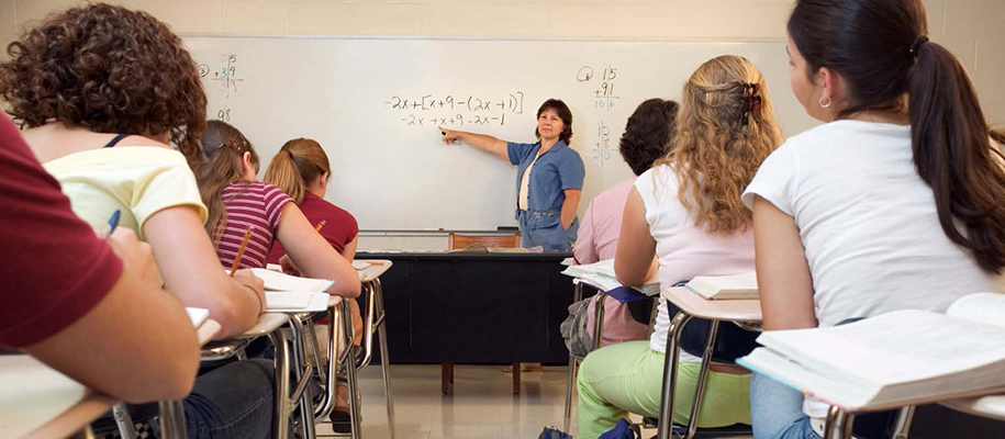 Female teacher in blue outfit teaching math to classroom of female students