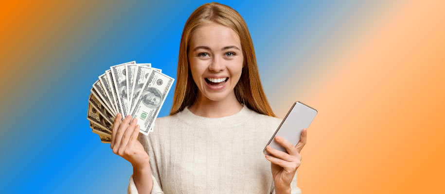 Young blonde female smiling, holding fan of $100 bills and smartphone