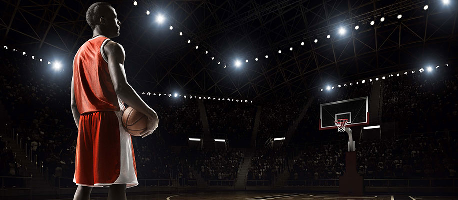Black male athlete holding basketball in dark arena with lights, looking at hoop