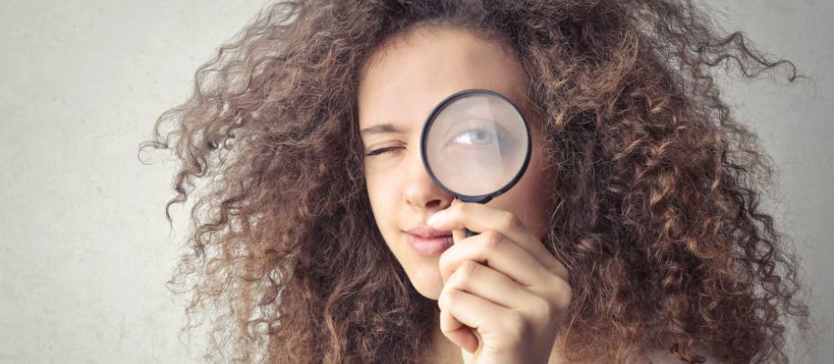 Young curly haired black female closing eye, looking through magnifying glass