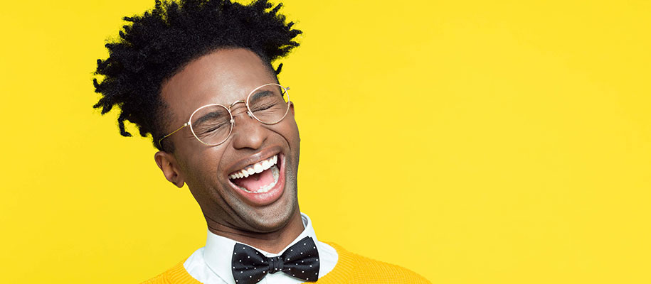 Black man in glasses and bowtie laughing with mouth open and eyes closed