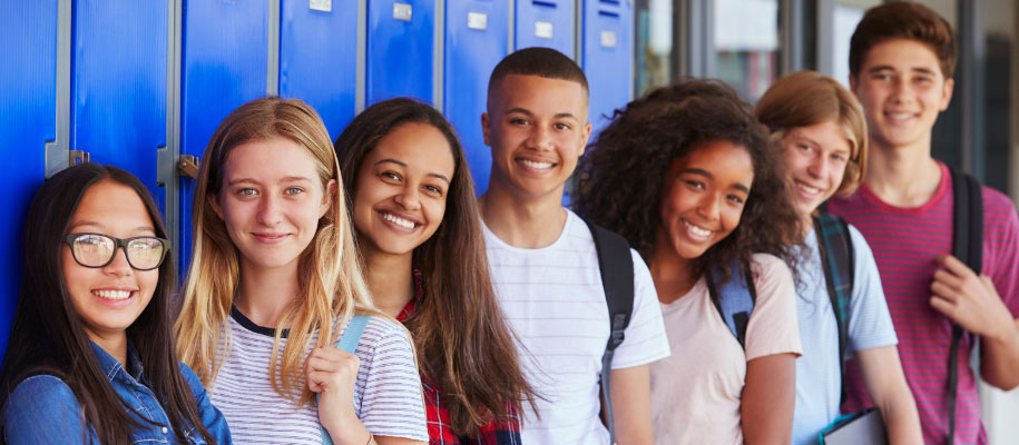 Row of diverse high school students smiling and standing against blue lockers