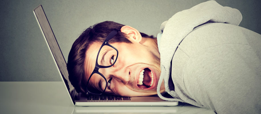 White male with brown hair & glasses, head lying against laptop keyboard yelling