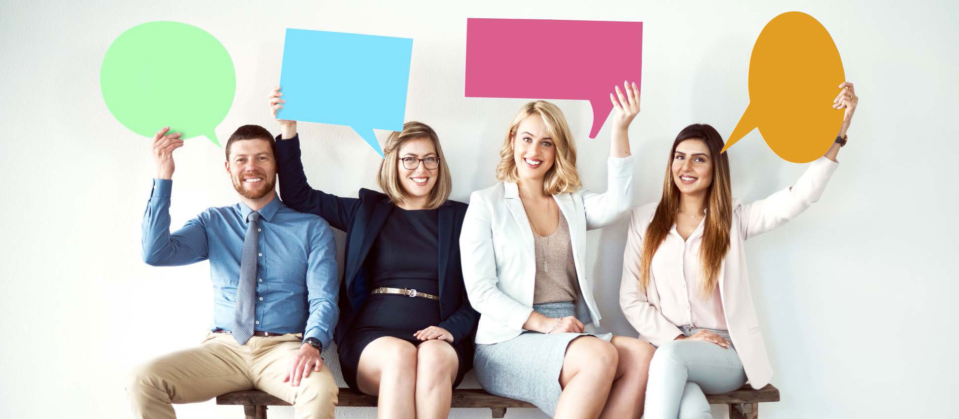 Four people in business attire on bench, holding big speech bubbles above heads