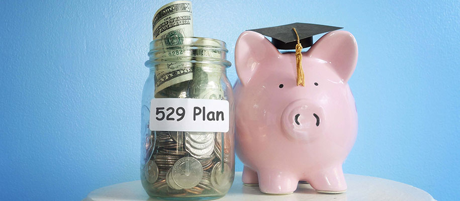 Piggy bank wearing small graduation cap next to money jar with 529 Plan label