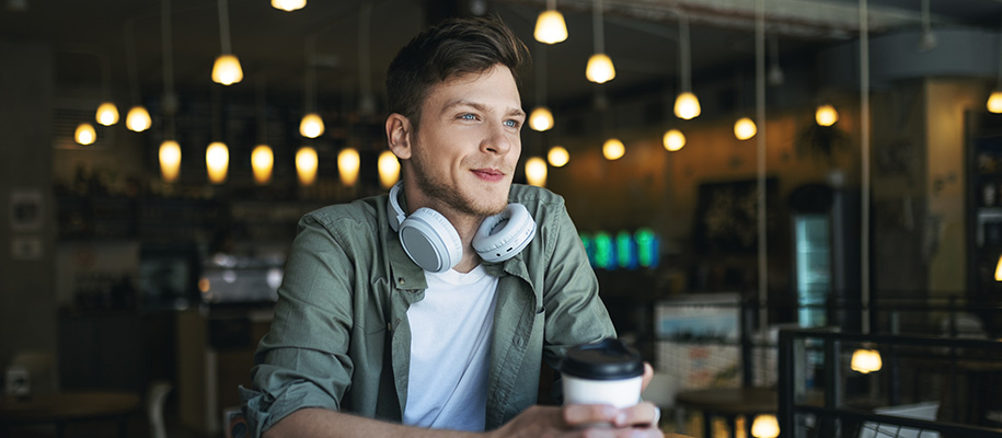 White man in green shirt with white headphones around neck smiling in coffee shop