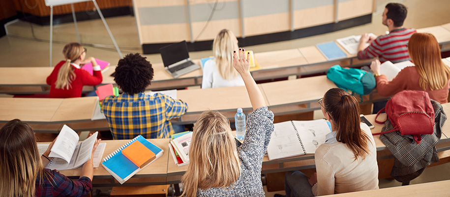 Diverse small class of students in lecture style room, one girl raising hand