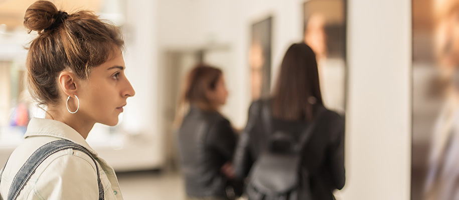 White woman with hoop earrings and bun looks at artwork in museum