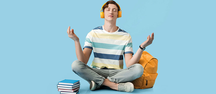 White male student sitting cross-legged in Zen pose with books and backpack
