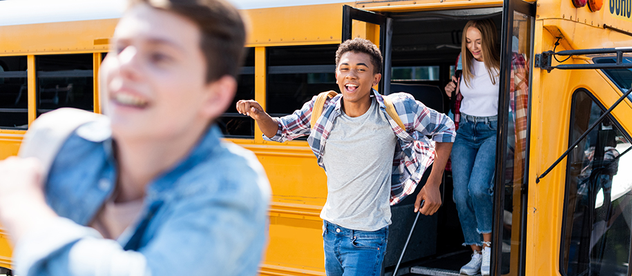Black male student happily leaving school bus between two other students