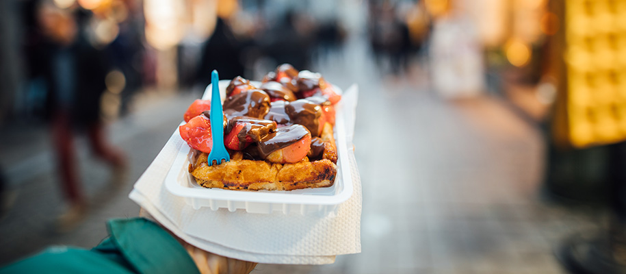 Coated arm holding out container of Belgian waffles in streets of Belgium