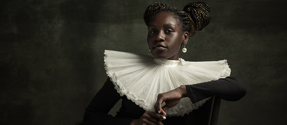 Black woman with braid buns in victorian ruffled collar looking right at camera