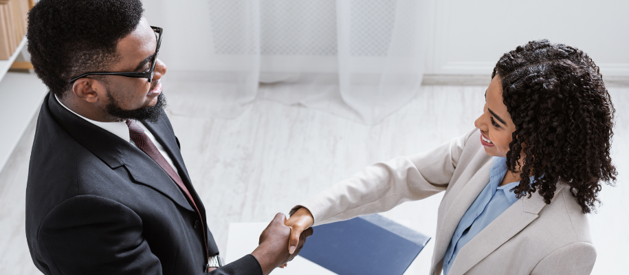 Overhead shot of Black man in suit shaking hands with Black woman in blazer