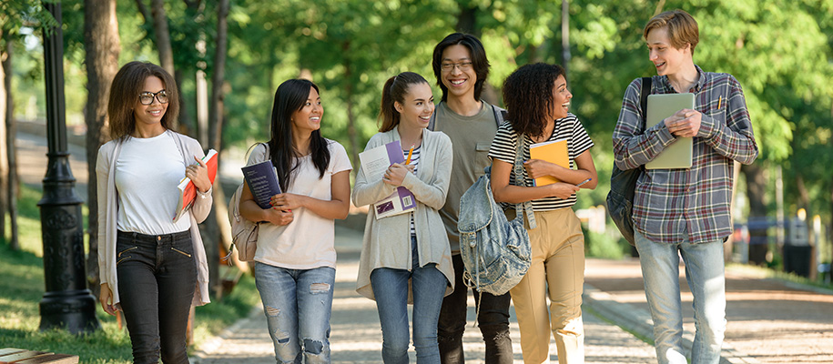 Diverse group of six students smiling, laughing with books, bags on campus
