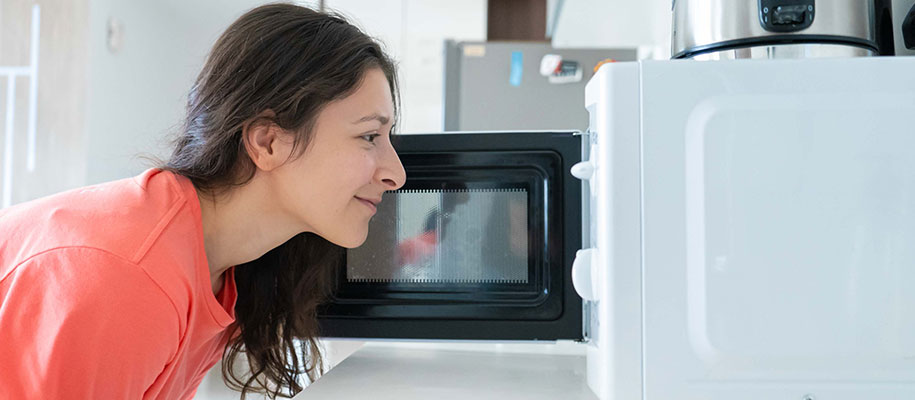 Side shot of brunette female looking inside microwave and smirking