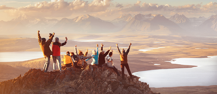 Large group of people on mountain peak with hands up in the air