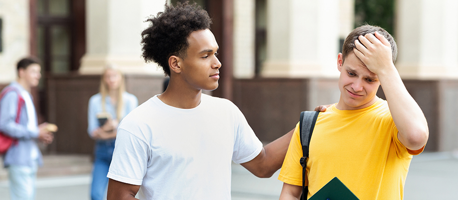 Black man in white T-shirt consoling White male friend in yellow shirt on campus