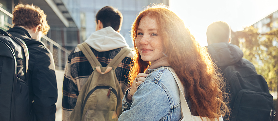 Young woman with red hair looking back at camera as male friends walk on