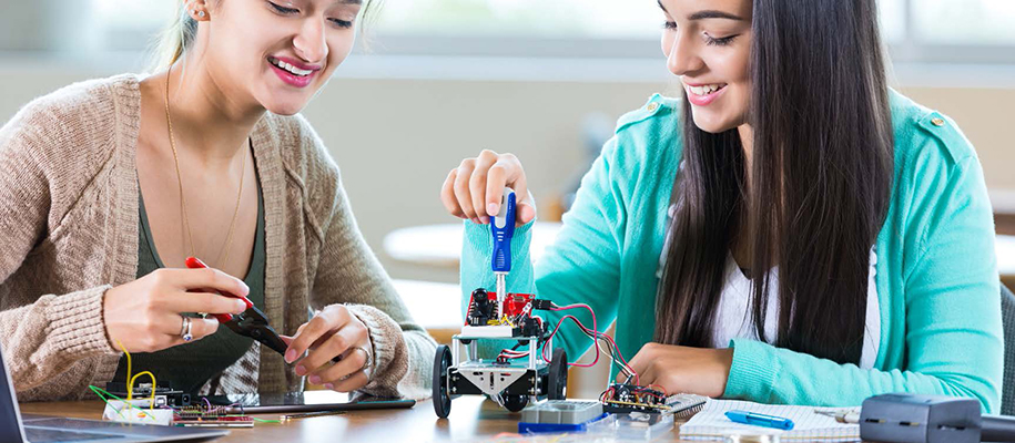 Two young women smiling and working on little robot vehicle with screwdrivers