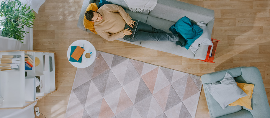 Brightly lit apartment with young White man on couch, focus on triangle pattern rug