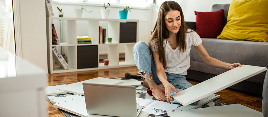 Young White woman on floor assembling white piece of furniture