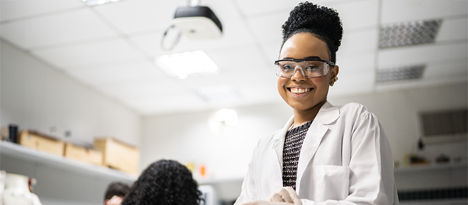 Young Black woman smiling in lab coat, striped shirt, lab glasses in laboratory